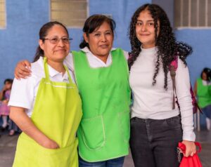 two-women-in-green-aprons-standing-next-to-a-young-adult-female-student