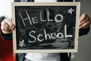 Student hands holding a small chalkboard with the words hello school written on it.