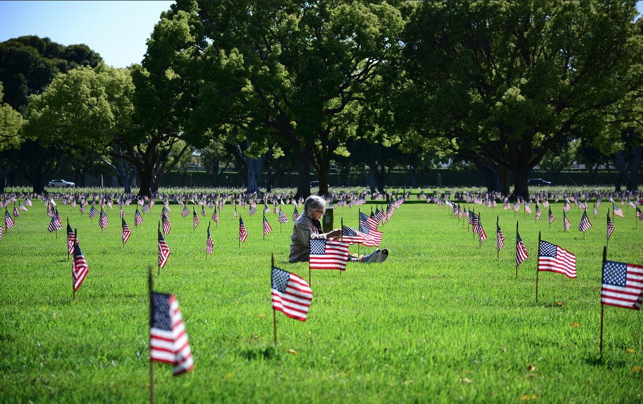 Woman sitting in a grassy field filled with American flags honoring fallen heroes for Memorial Day